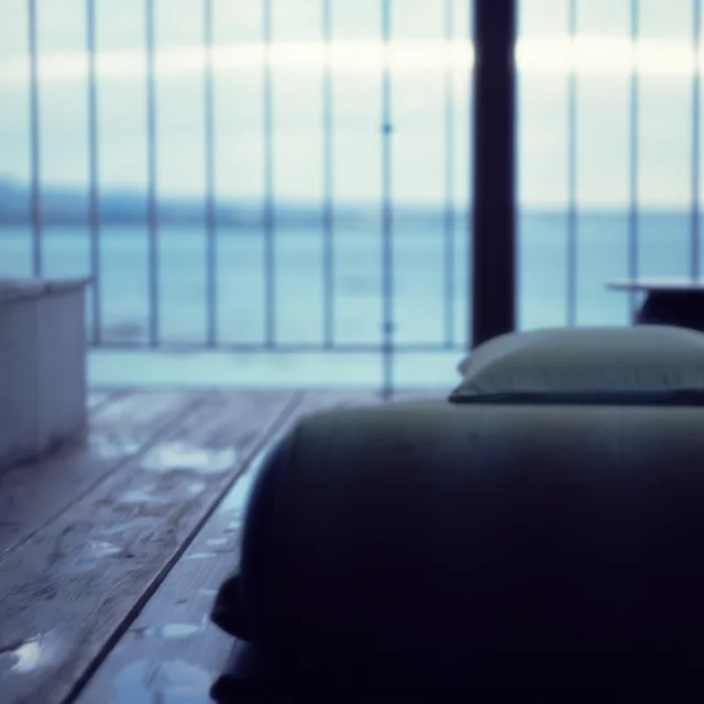 A bed and pillow beside large windows overlooking the sea