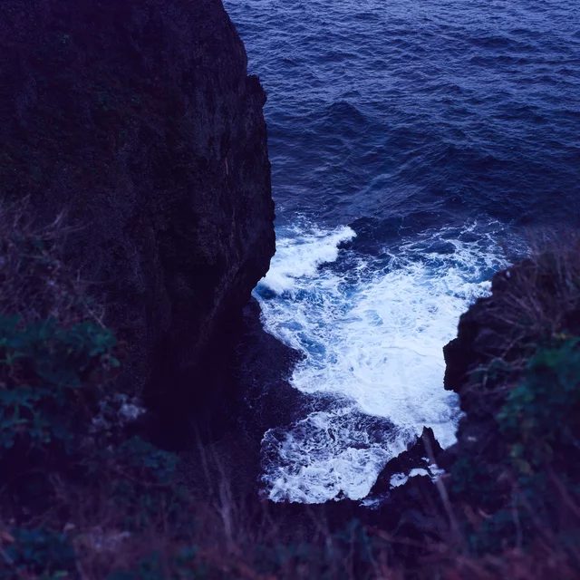 White waves breaking in a narrow gap between dark coastal cliffs