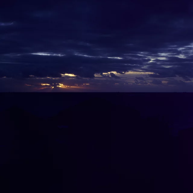 A narrow band of sunset light beneath layered dark blue clouds