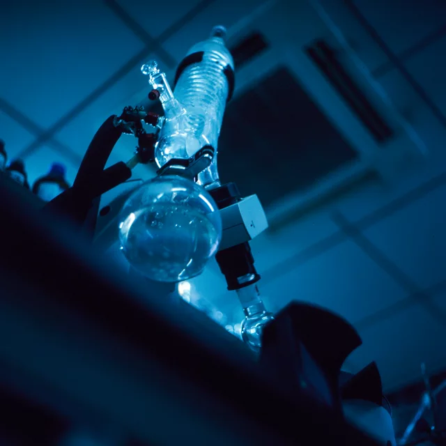 A round-bottom flask and glass condenser illuminated by blue light in a laboratory